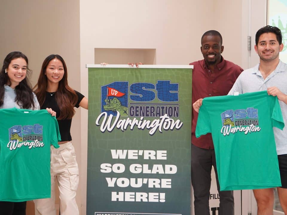 Three first generation students with Jeff Danso by a 1st Generation Warrington sign that says We're so glad you're here! Two students hold up similar t-shirts.