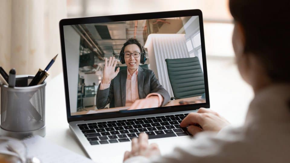 Person using a laptop with a screen showing someone in a virtual meeting