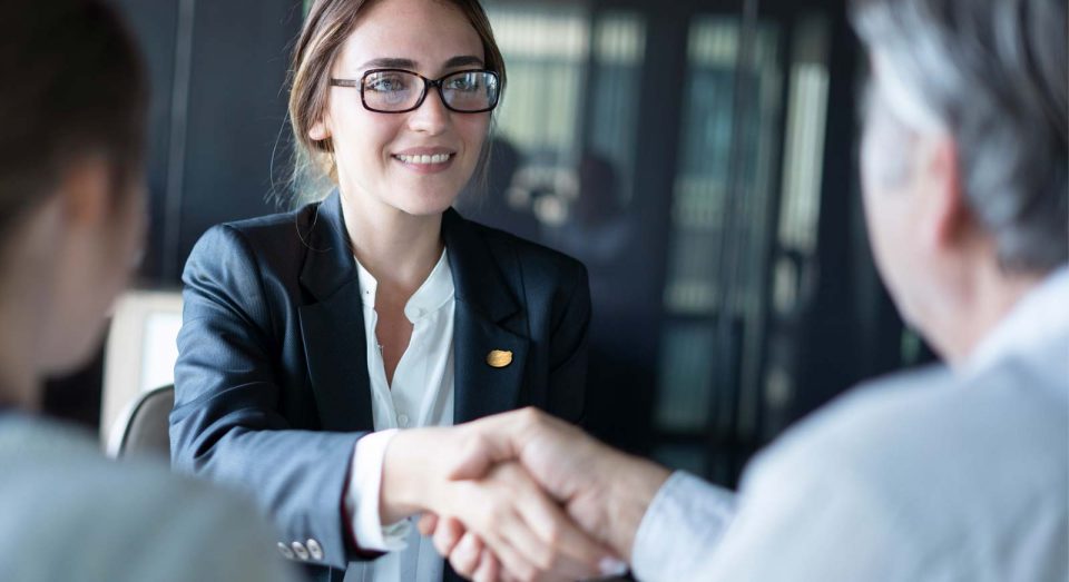 Young woman in business attire wearing a Gator lapel pin shakes hands with a business professional