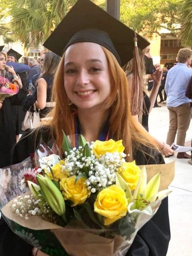 Agustina Vincent de Urquiza in cap and gown holding flowers after graduation