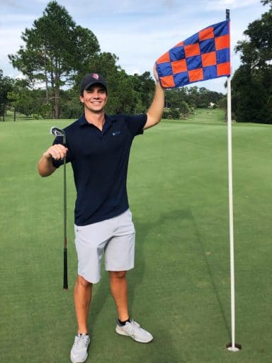 Samuel Nunner holds an orange and blue checkered flag marker at a golf course