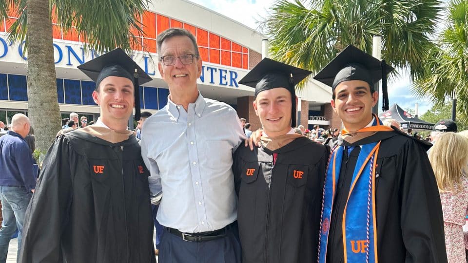 David Brown with three students in caps and gowns outside of the O'Connell Center after the ceremony