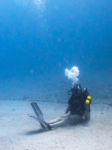 Jacqueline Digiorgio in scuba gear sits on the floor of an ocean
