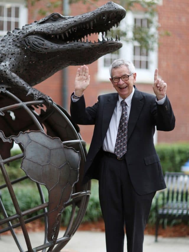 Wayne Archer smiles by the Gator Ubiquity Statue and holds up his hands with a number one gesture