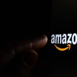Amazon logo lighting up a person's pointer finger with a black background