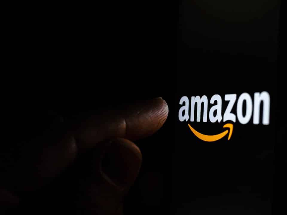 Amazon logo lighting up a person's pointer finger with a black background