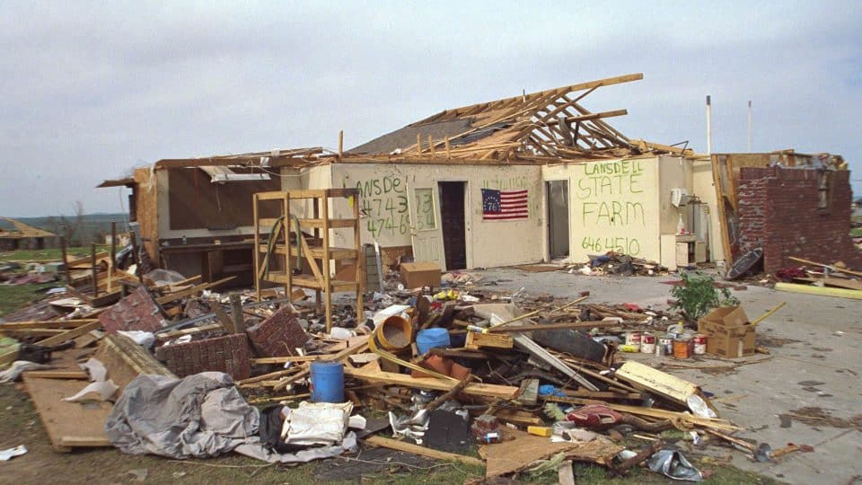 A building with its roof destroyed and spray painted information on the walls while storm debris is all around