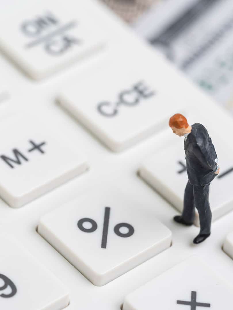 A small figure of a man stands on a calculator looking at the percentage key