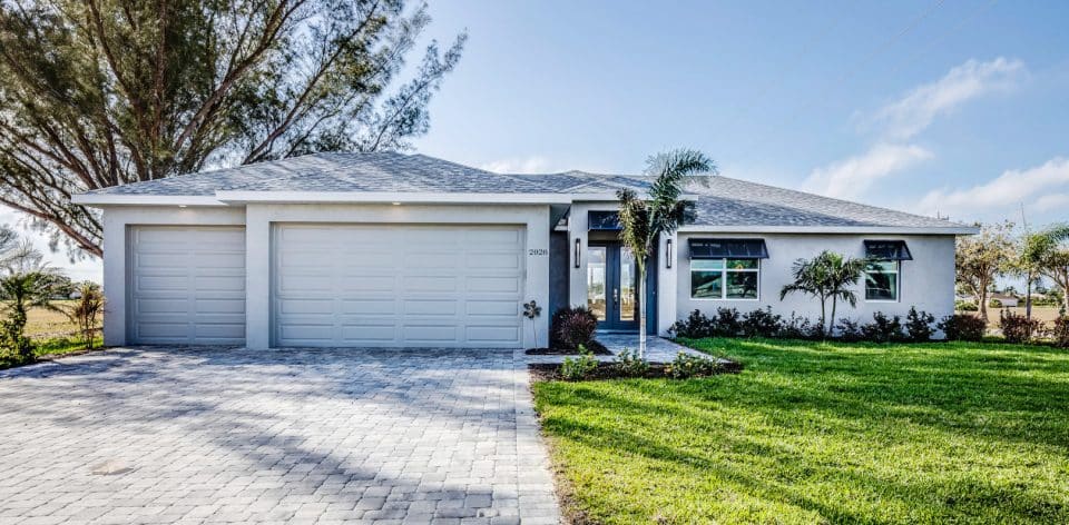 A new home in suburban Florida with a three car garage, paver driveway and grassy yard with landscaping