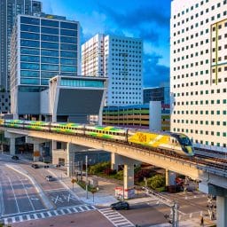 A passenger train departs MiamiCentral on an elevated track with tall buildings all around