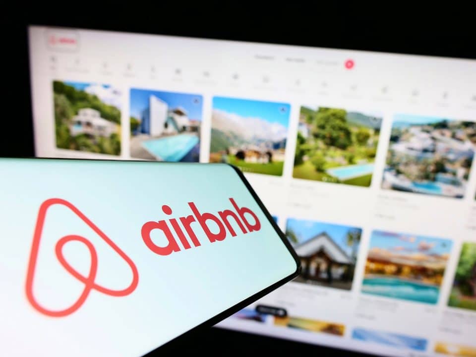 airbnb logo in the foreground with its website in the background showing many listings
