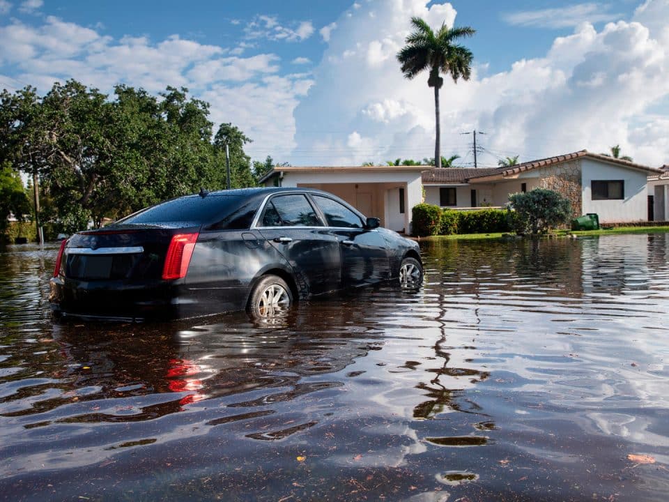 A car sits in water halfway up its tires near a home