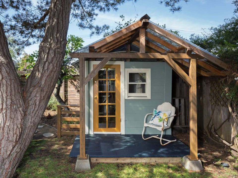 A small accessory dwelling unit in a backyard with a chair on the front porch