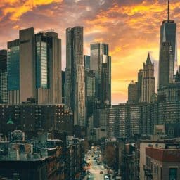 Looking down a street in New York City from a high vantage point with tall buildings and orange clouds in the background