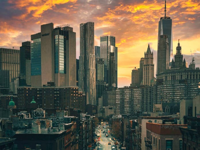 Looking down a street in New York City from a high vantage point with tall buildings and orange clouds in the background