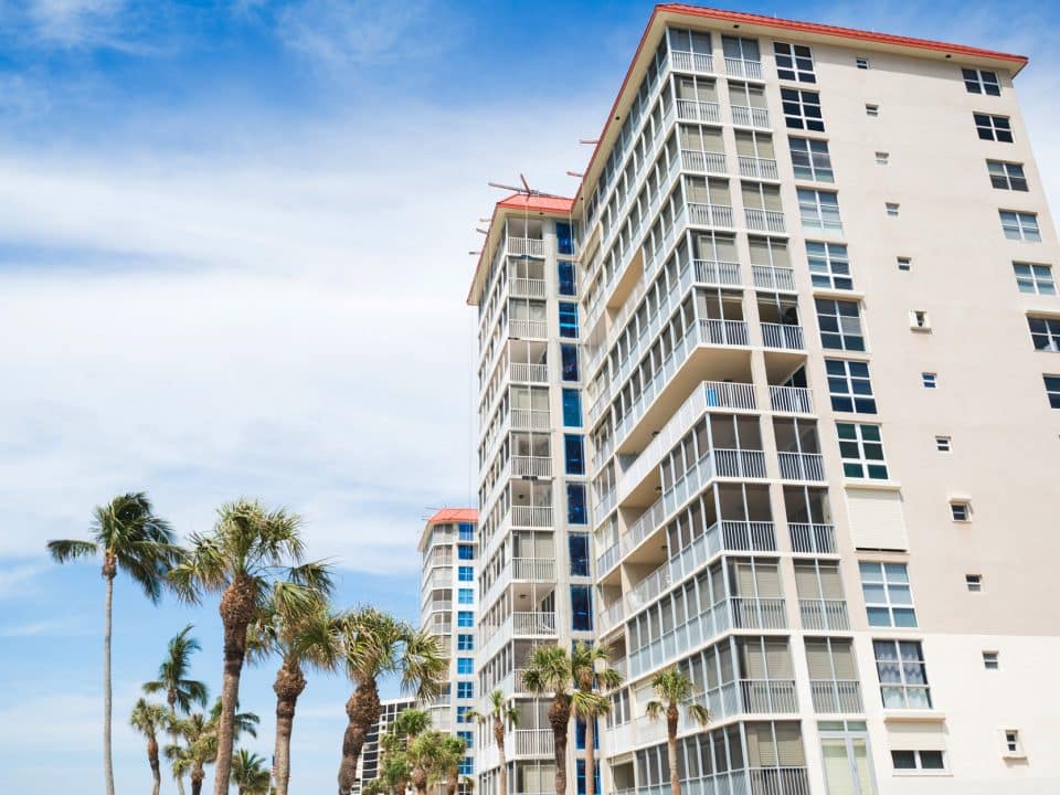 Tall condos with palm trees and wispy clouds on a blue sky