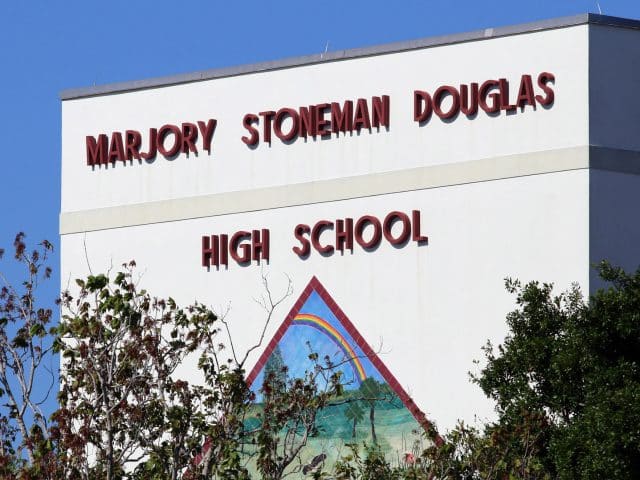 The name Majory Stoneman Douglas High School on the outside of the building with some artwork below it and trees in the foreground