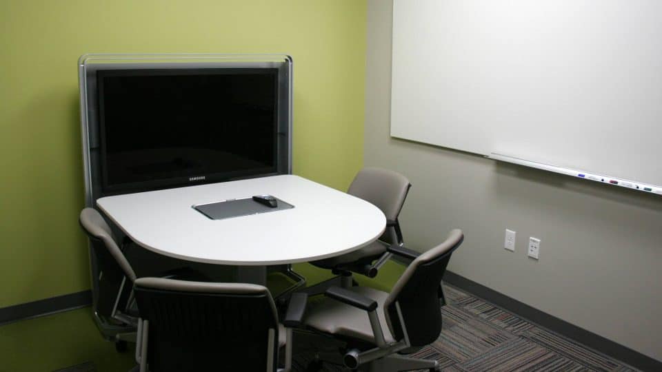A room with a small table, a large monitor and a whiteboard