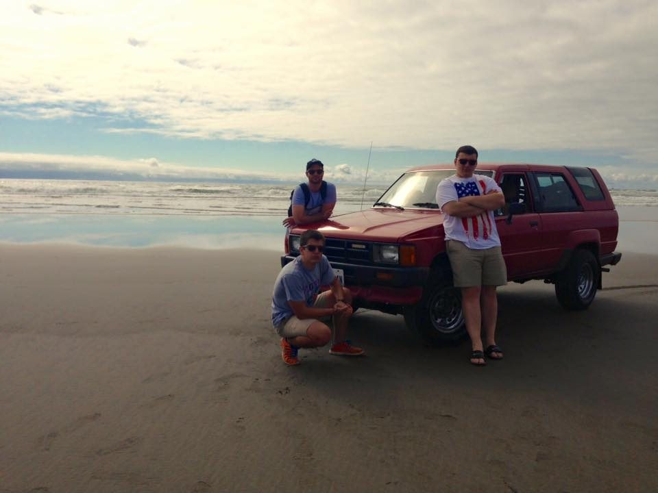 Three FLA students on the Pacific Ocean beach with a red vehicle