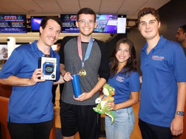 Four ambassadors at a bowling alley while three hold prizes and one is wearing a medal