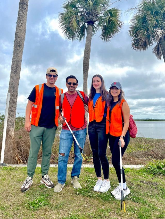 Four ambassadors with orange vests on while two hold litter grabber tools