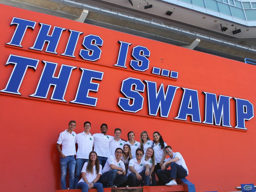 Group of HLC students in the Ben Hill Griffith Stadium under This is... the Swamp text on wall