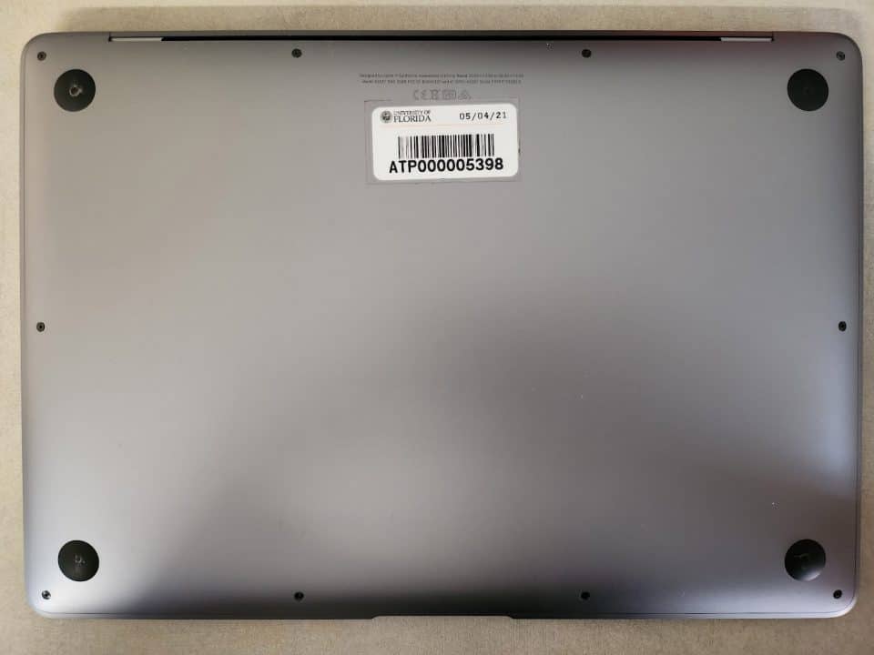 The bottom side of a laptop computer with a UF decal with a bar code and ID number