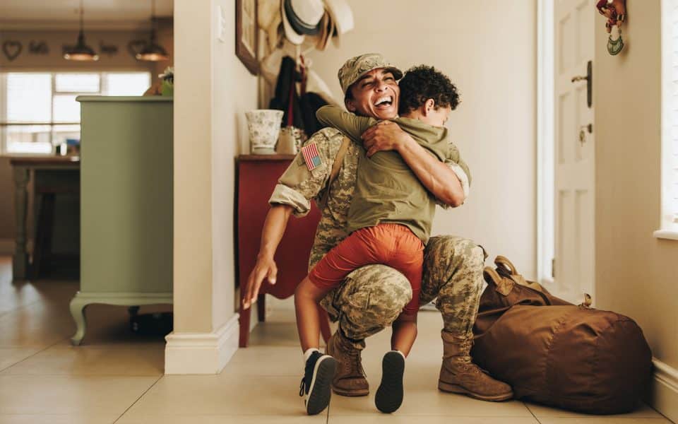A child hugs a kneeling soldier inside a home by the front door