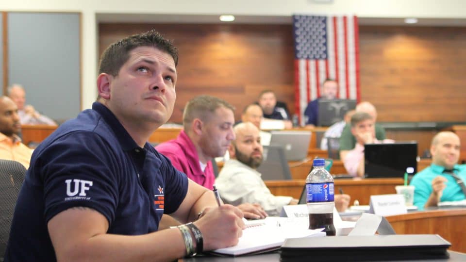 A man looks up at the presentation with other students and a U.S. flag on the wall in the background