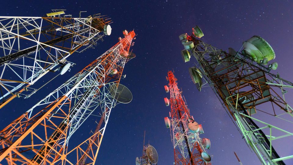 Five telecommunication towers from the ground looking up into the night sky