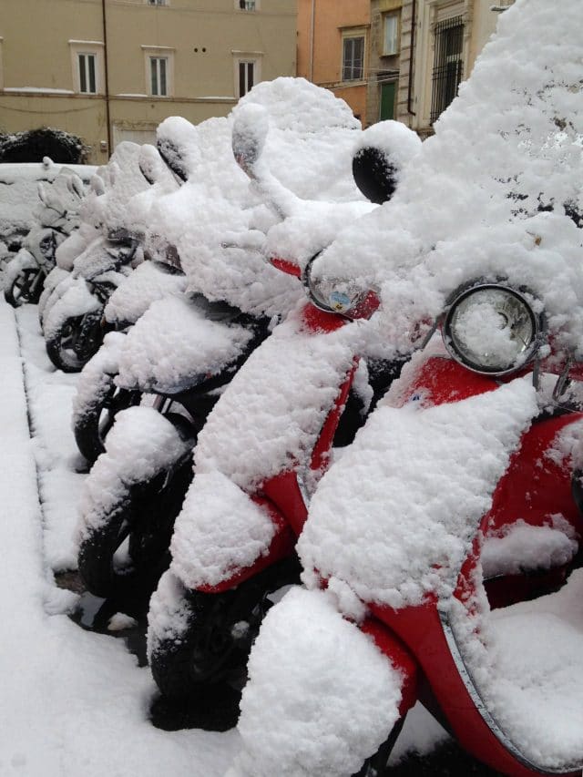 Scooters covered in snow line a street in Rome, Italy