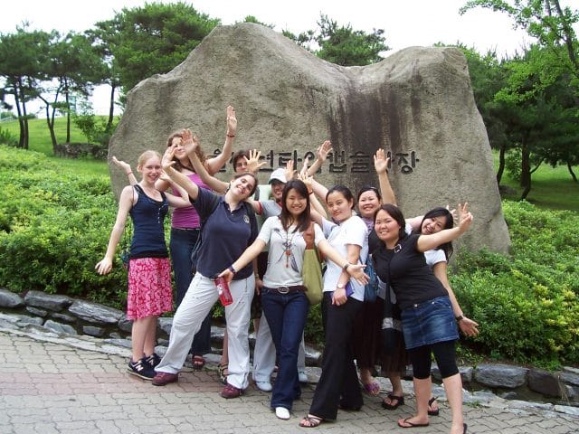 Students of different nationalities stand in from of a rock with writing on it in South Korea