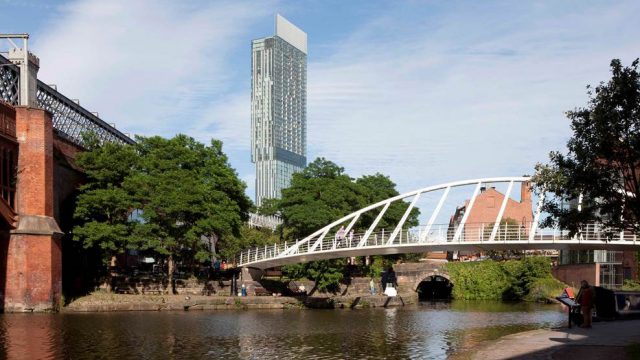 A skyrise with a walking bridge over water in Manchester, England