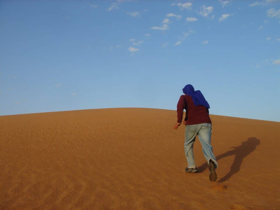 A young man runs up a sand dune in a Moroccan desert