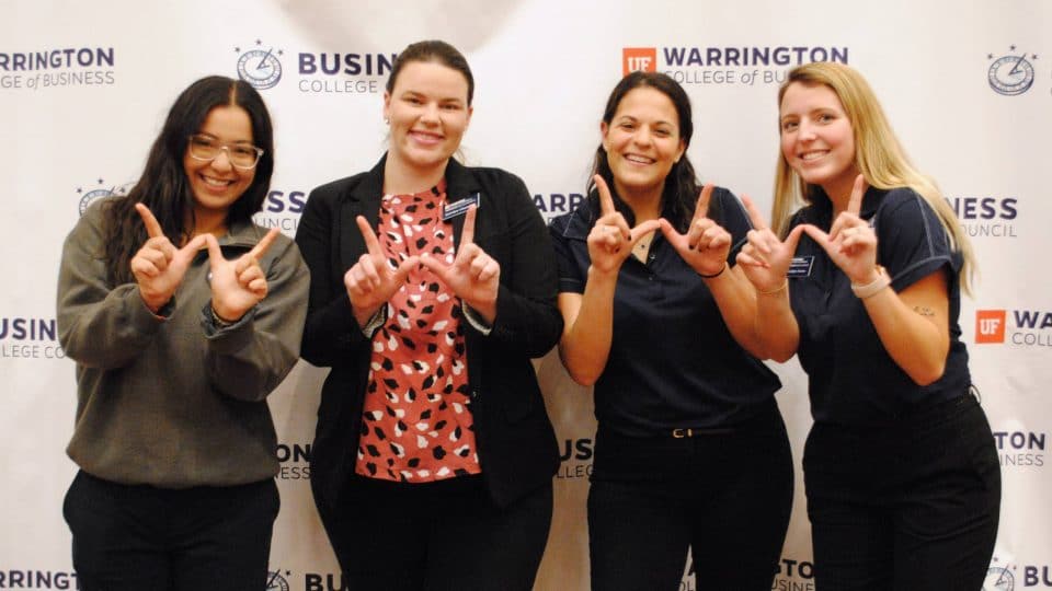 Four female Warrington Welcome students holding their fingers in the shape of a W
