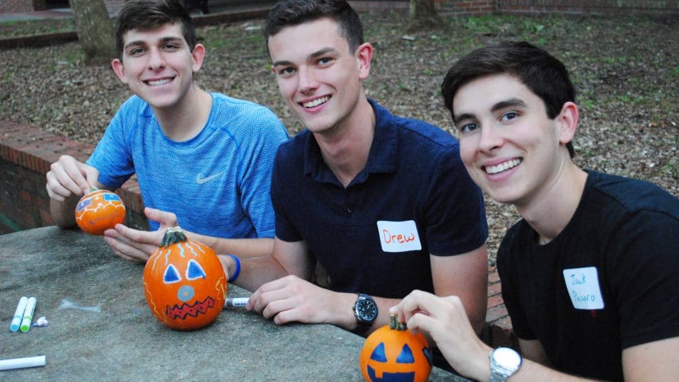 Three male Warrington Welcome students decorating pumpkins with markers