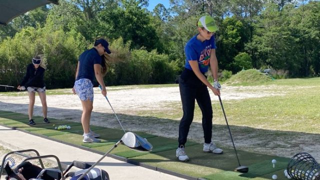 Three women practice their golf swings